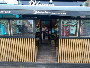 From pavement facing venue. Path to entrance proceeds between wooden dividing walls ahead.