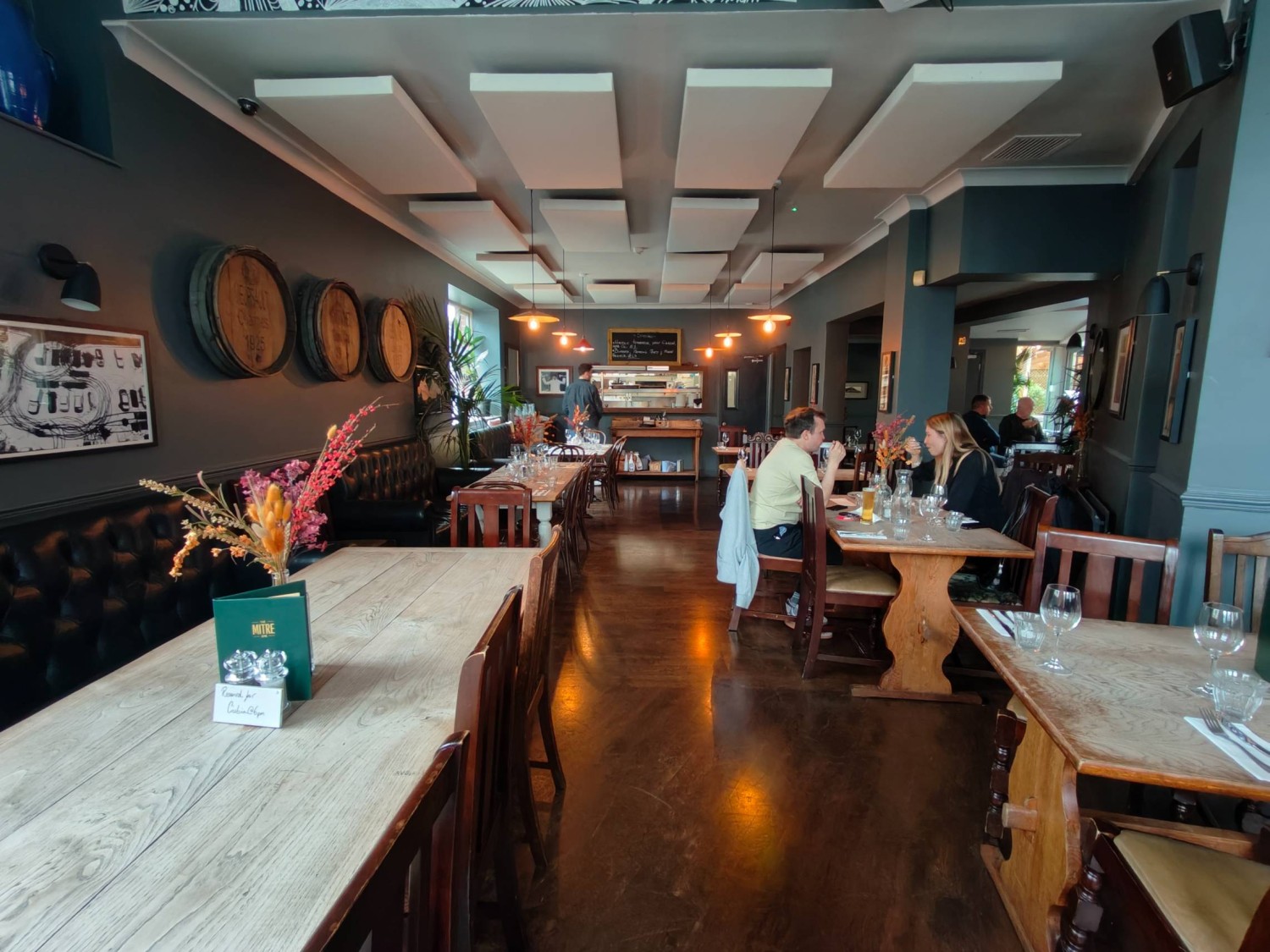 From end of right side path looking straight. Half booths along left. Path in centre. Open kitchen along back wall. Table and chairs along right.