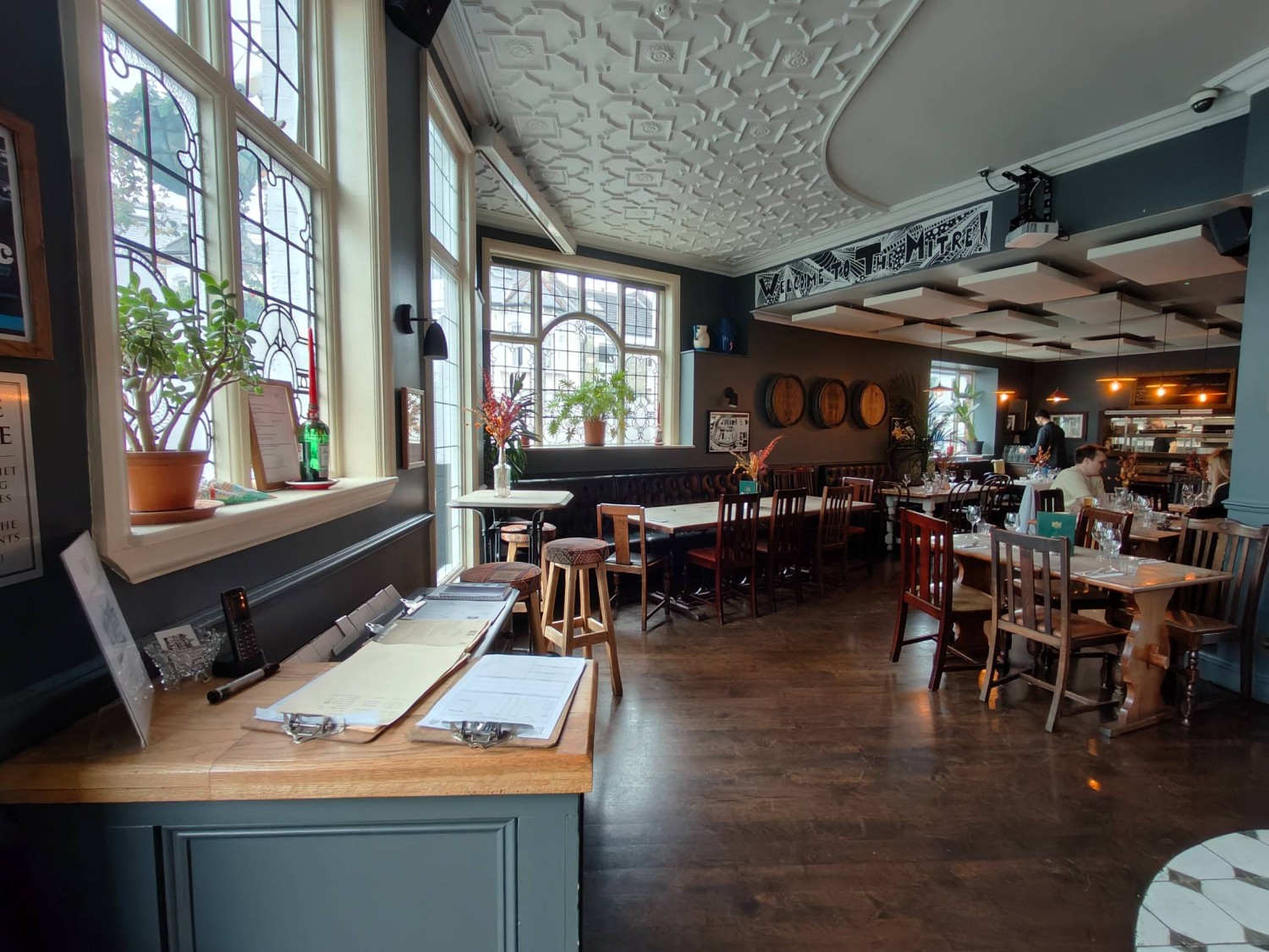 From entrance facing right. Counter on left. Stools along left. Path in centre going right to half booths along back and table and chairs on right.