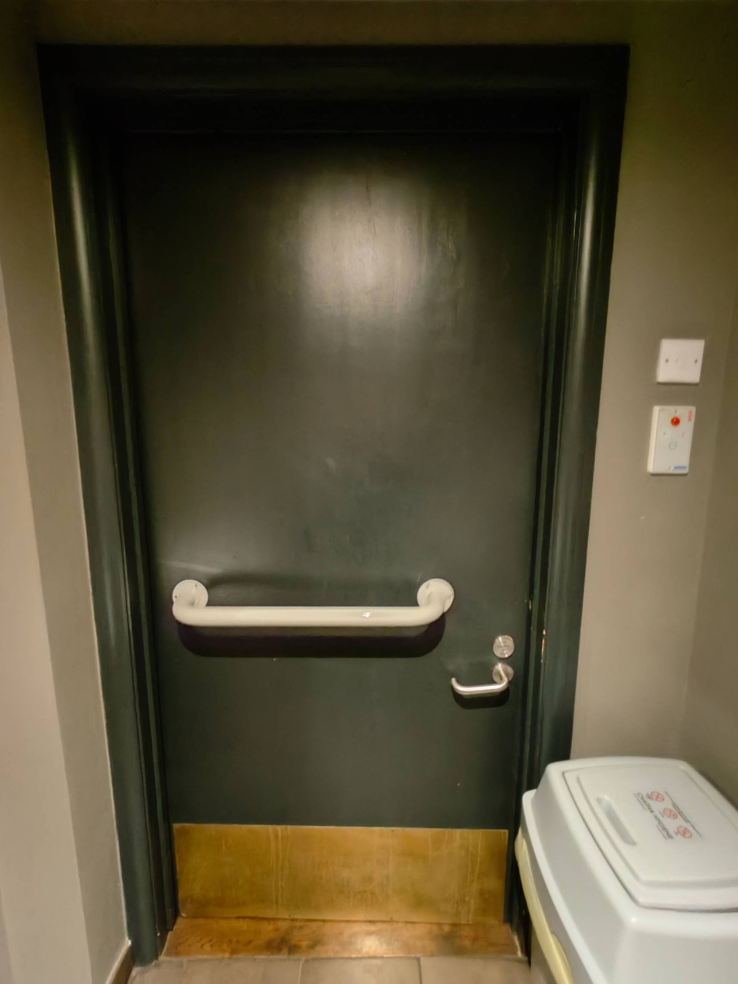 From toilet facing straight towards back of toilet door. White grab rail in centre. Push silver handle on right to open.