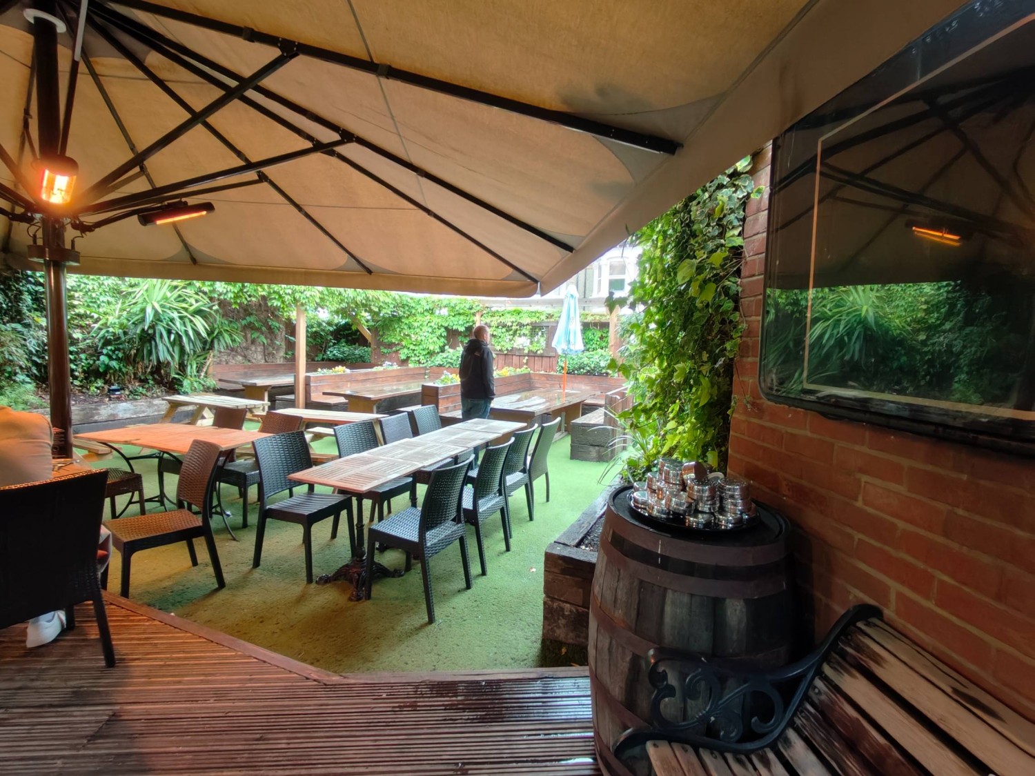 From door facing straight. TV and bench on right. Path ahead leads to tables & chairs in back centre. Picnic tables on back left. Booths on back wall.