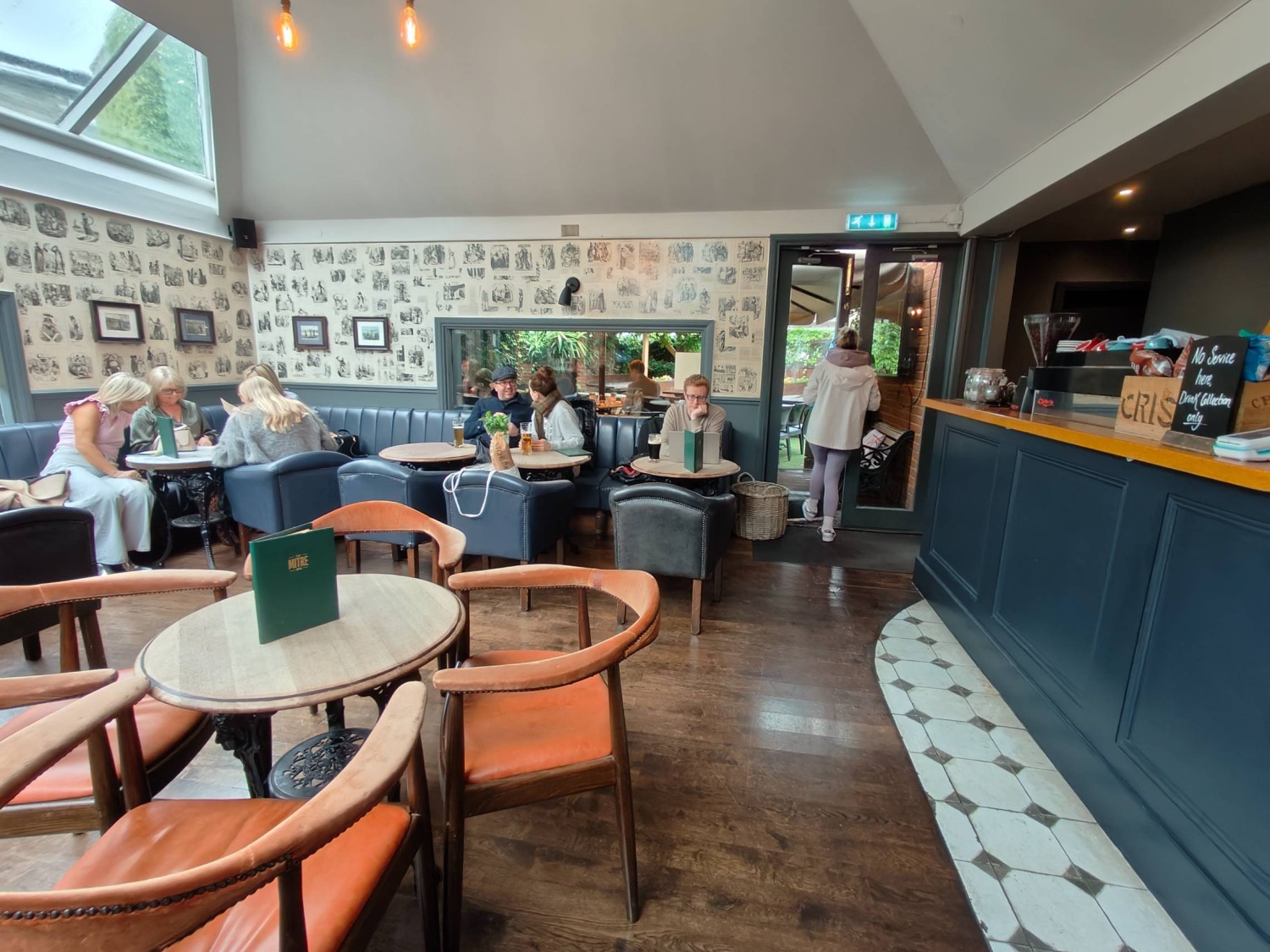 From end of path left of bar looking right. Table & chair on left. Half booths at back. Path on right leading to outdoor side area. Bar on far right
