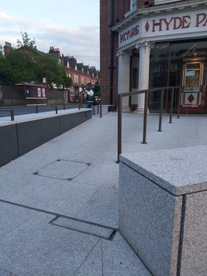 Concrete ramp leading up to main entrance. It is split down the middle by metal handle rail, with ample space on each side for various sizes of chairs