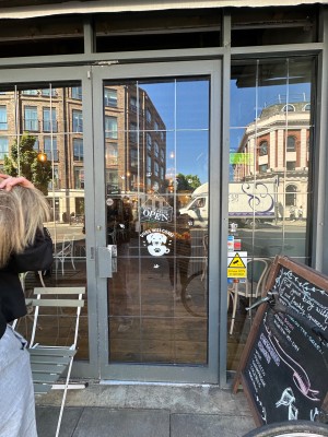 Glass door with grey metal frame. Push from handle on left to open.