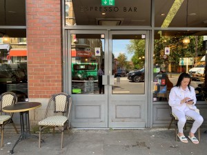 From street, facing entrance. Path down center to entrance doorway ahead. Outdoor seating on left and right of doorway.
