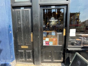 Single glass door with black wooden frame. Push gold metal panel on right to open.