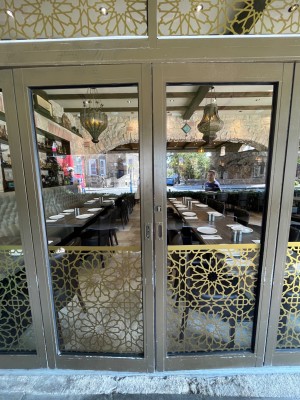 From path through outdoor area facing right. Double glass doors in brown plastic frame. Requires staff to open. Doors fold open from centre.
