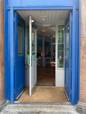 Blue double wooden doors. Push from center to open. Single grey wooden door immediately after. Pull from silver metal handle on right of door to open.