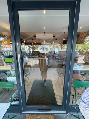 Single glass door with grey metal frame. Push long silver metal handle on left to open.