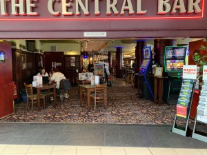 Wide open archway ahead. Menu stands slightly obstructing entrance on right. Tables and chairs immediately after entrance on left.