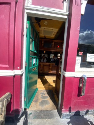 Green wooden door, with glass panel. Push on right to open.