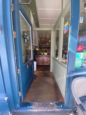 Glass door, with blue wooden doorframe. Gold handle on right. Push to open.