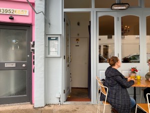 From street, facing entrance. Path straight to entrance door ahead. Outdoor seating to right of entrance door.