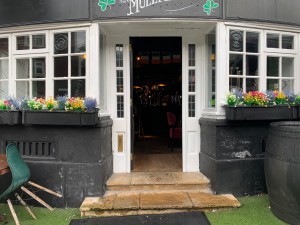 From street, facing entrance. Outdoor seating to left and right of path. Path straight to entrance door ahead.