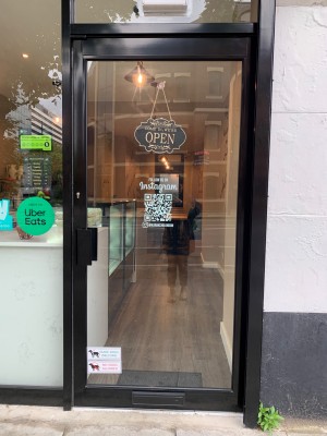 Glass door with black metal frame. Push from black metal handle on left of door to open.