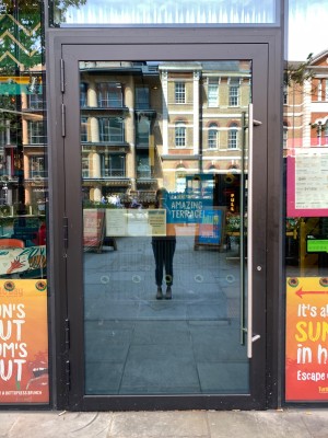 Glass door with black metal frame. Pull from silver metal handle on right of door to open.