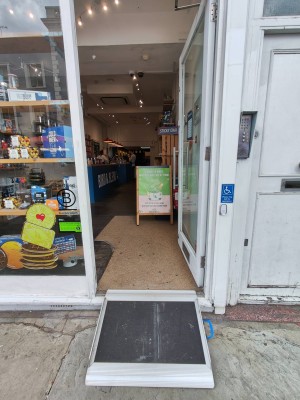 White framed door. Push silver handle on left to open. Doorbell for assistance to right of door.