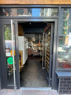 Single glass door with black frame. Push vertical metal handle on left to open.
