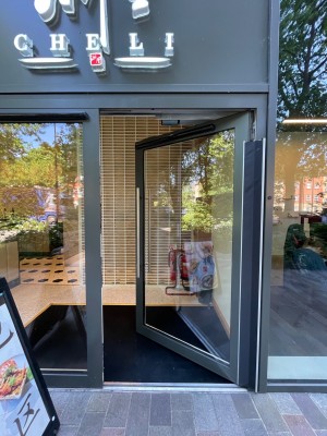 Single glass door with black frame. Push vertical metal handle on left to open.