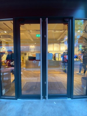 Double glass door, with black doorframe. Handles at centre of door. Push to open.