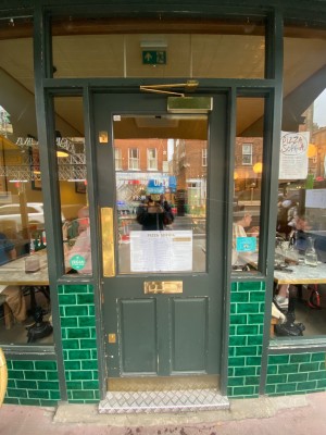 Green wooden door, with glass panel. Push on left to open.