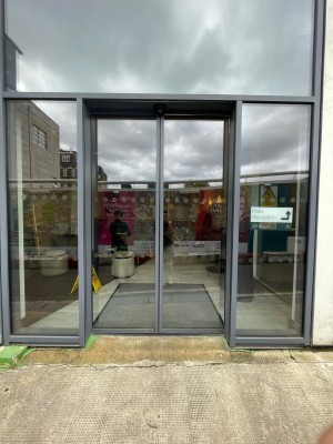 Double glass doors in black metal frame. Slide open from center. Approach to automatically open.