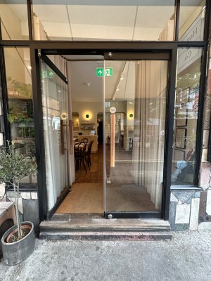 Glass panelled doors with black doorframe. Wooden vertical handles in centre of doors. Push to open.