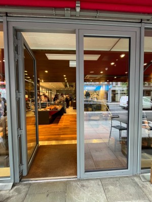 Single glass door in grey metal frame. Silver metal handle. Push from right to open.