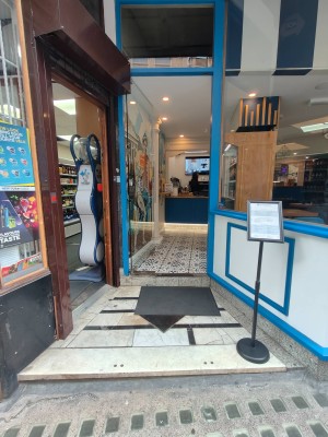 Path ahead to entrance door. Glass door with blue wooden frame. Push handle on right to open.