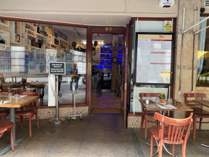 From street, facing entrance. Path straight to entrance door ahead. Outdoor seating to left and right of entrance door.