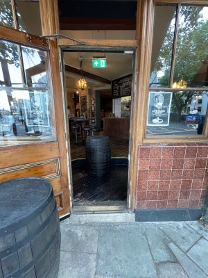 Single wooden door with glass panel. Pull golden handle on right to open. Barrel on left propping door open.