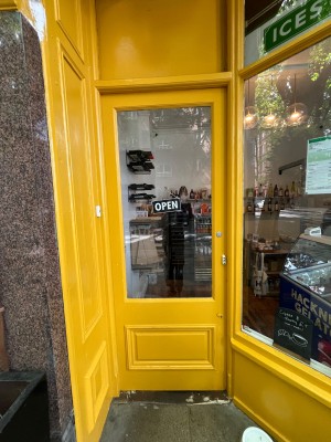 Yellow door with glass panels. Push from right side to open. Doorbell for assistance on left of frame.