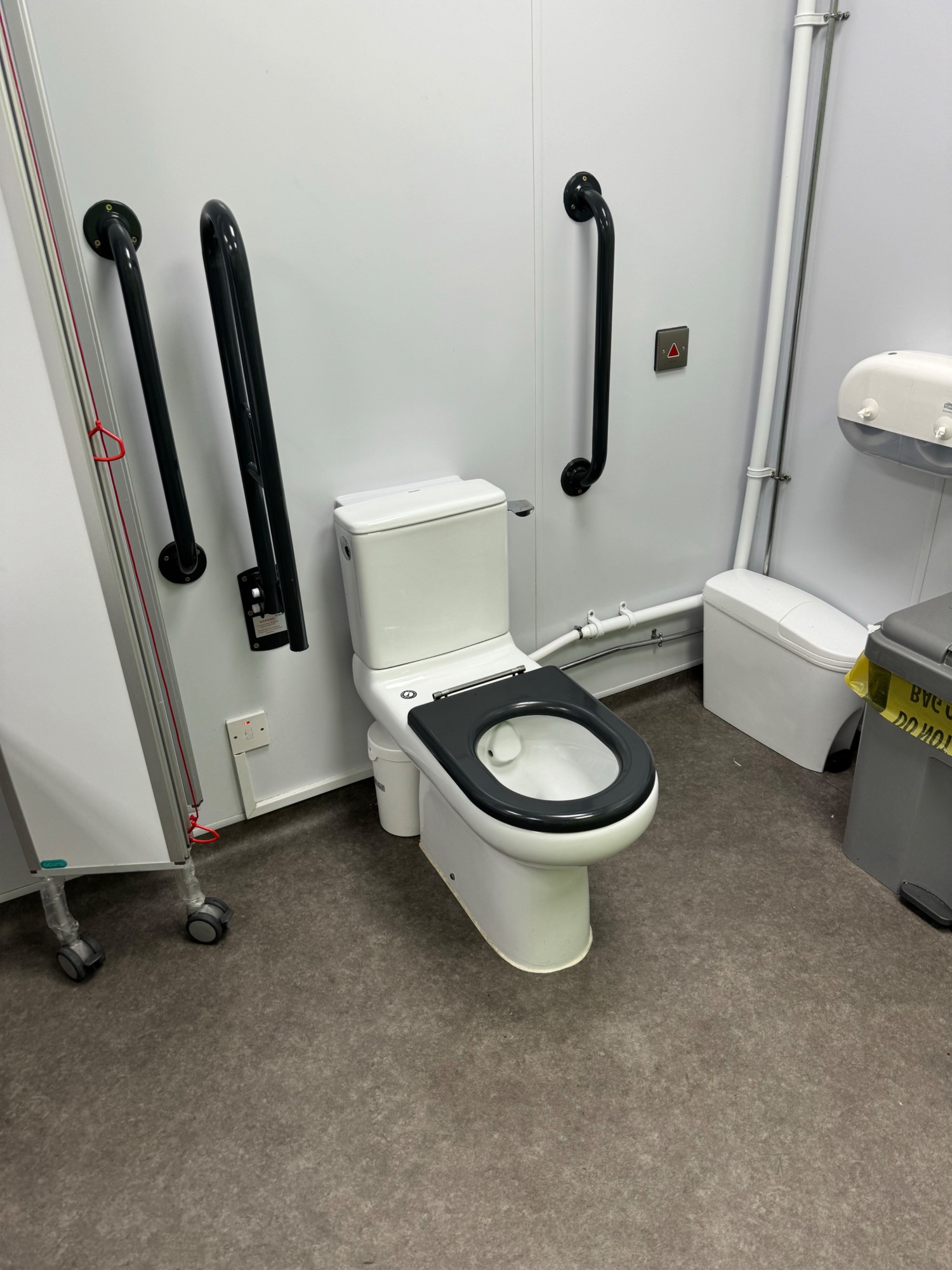 Toilet with hand rails both sides and screen that devides the toilet from the rest of the room
