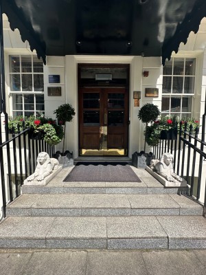 From pavement looking straight at steps leading up to double doors on back wall ahead. Statues to left and right at top of stairs.