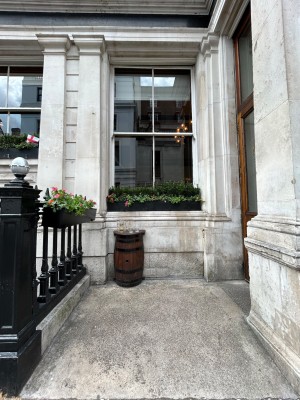From left of main entrance, facing venue. Ramp ahead leads to alt entrance on right. Table on back left.