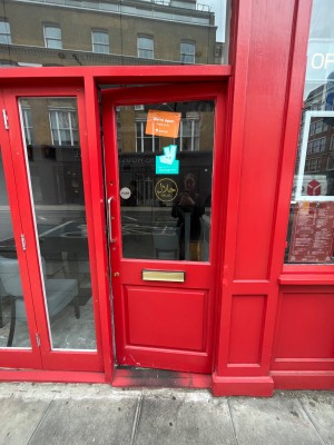 Single red wooden door with window ahead. Push silver metal handle from left to open.