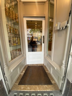 Glass door, with white wooden doorframe. Handle on right. Push to open.