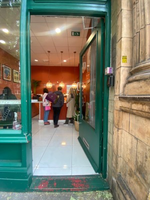 Glass door, with wooden green doorframe. Silver handle on left. Push to open.
