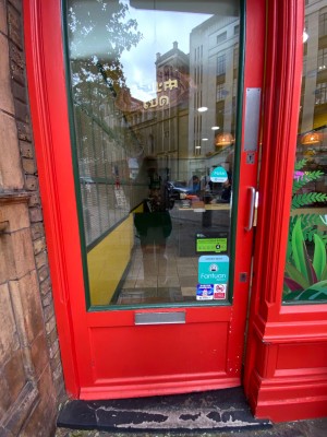 Glass door, with red wooden doorframe. Silver handle on right. Push to open.