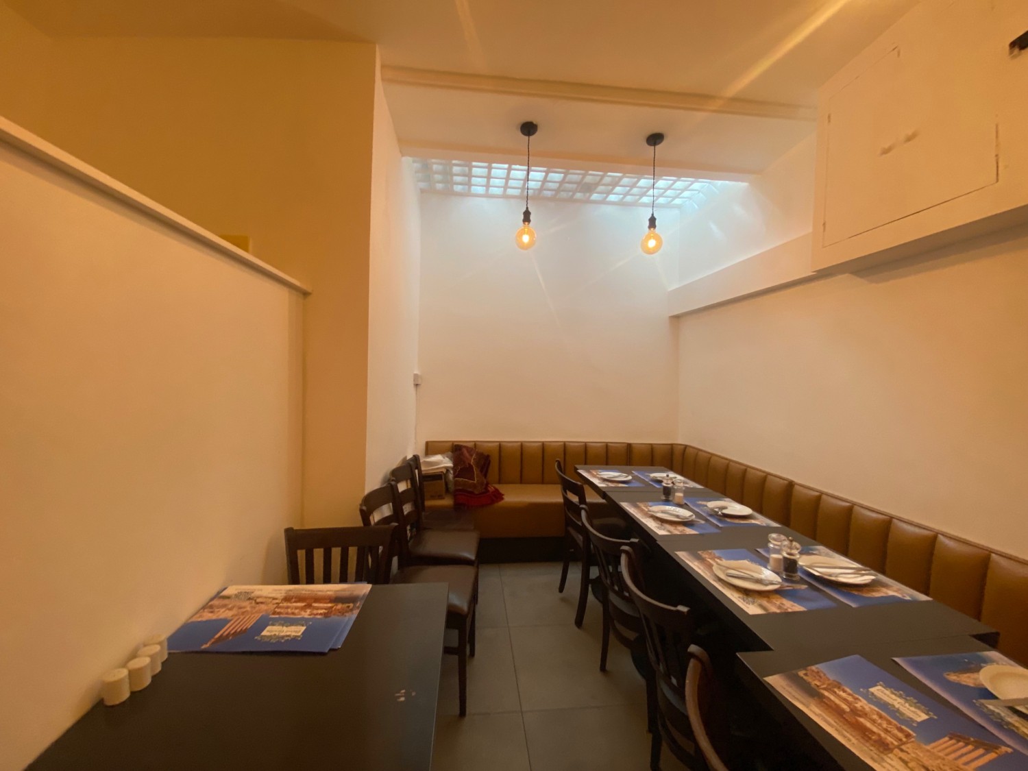From wall divider, facing straight. Tables and chairs along left. Half booth, tables and chairs along back and right walls.