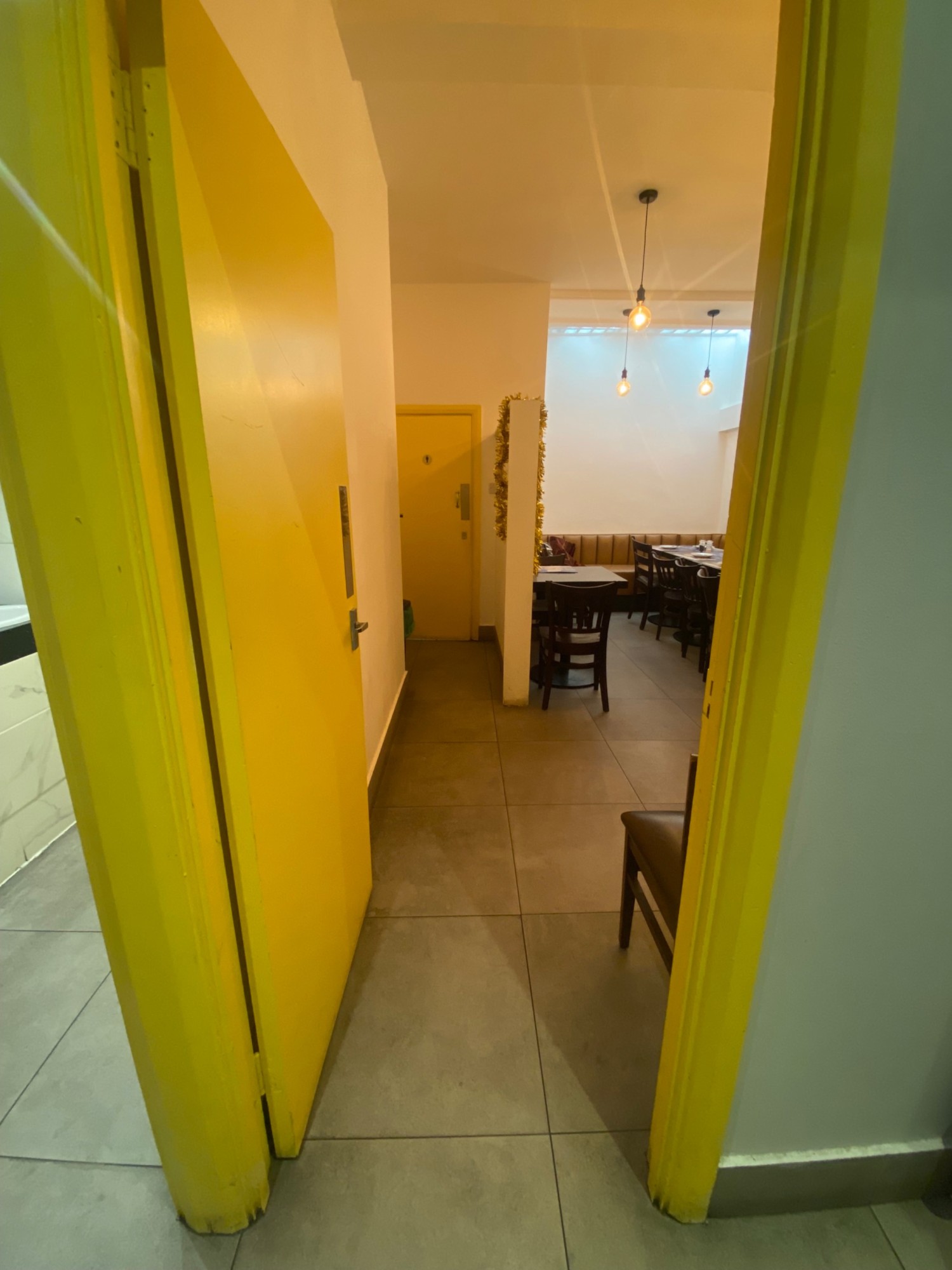 From bottom of second flight of stairs, facing right. Door to downstairs area in front. Yellow wooden door, silver handle on right. Push to open.