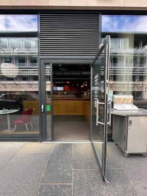 Glass panelled door with black doorframe. Vertical silver handle to left of door. Pull to open.