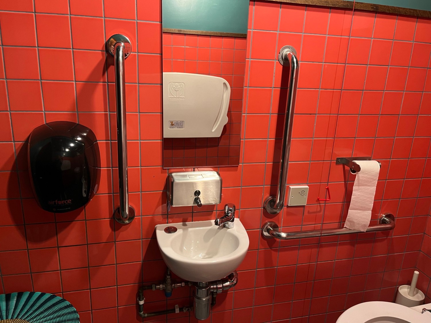 The sink is in the centre, with a soap dispenser above and a hand dryer on the left.
