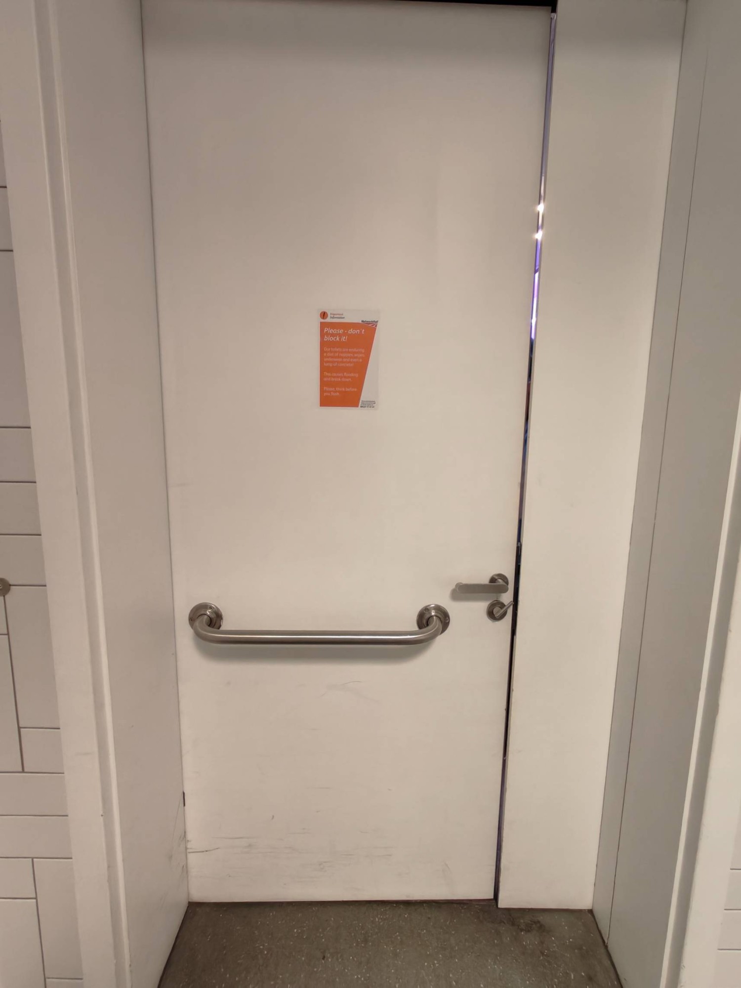From right of sink facing back of toilet door. Silver grab rail in centre. Push handle on right to open.