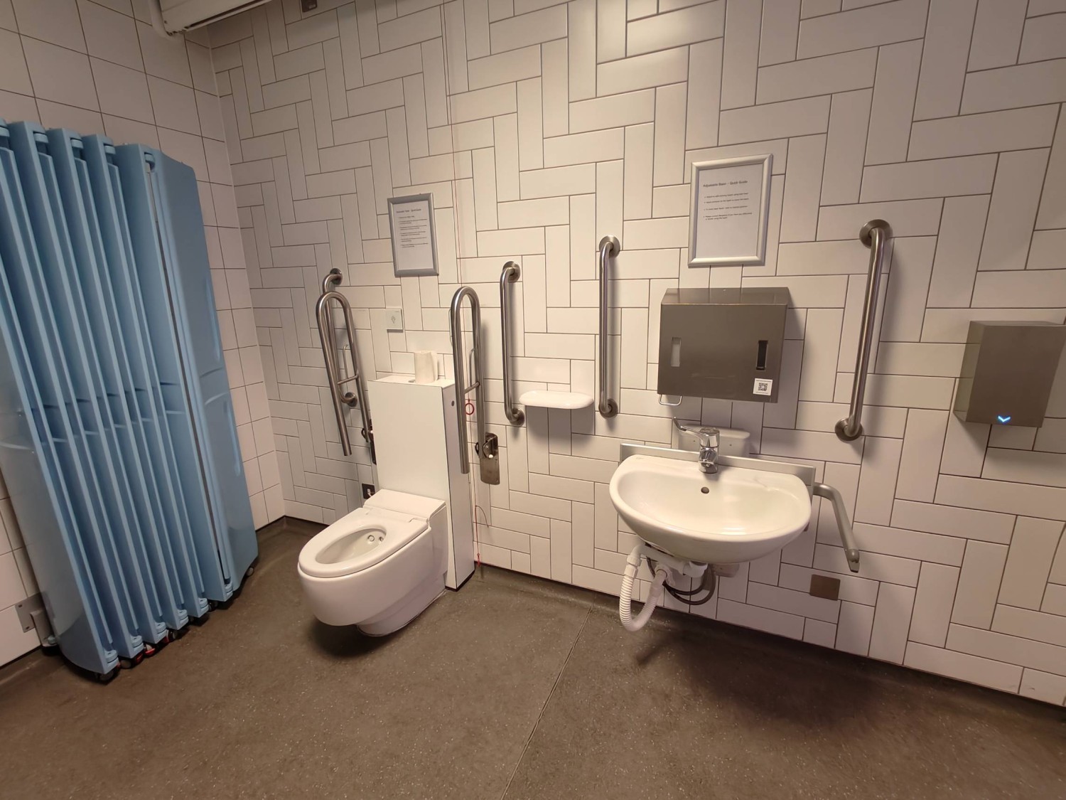 From changing table facing right. Divider on far left. Toilet on left. Sink along back wall.