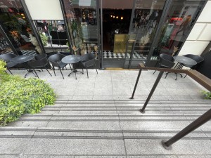 From pavement in front of venue facing straight. Stairs down to entrance ahead. Black metal handrail to right.