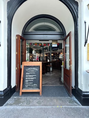 Archway precedes sliding brown wooden door with glass panels on left and single wooden door with glass panel on right. Notice board on left.