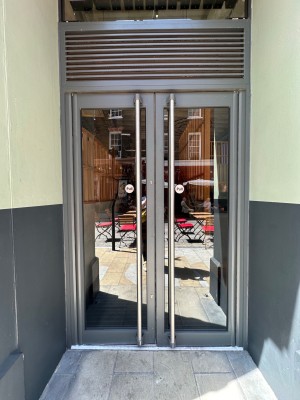 Glass doors with grey doorframe. Silver vertical handles in centre of doors, pull to open.