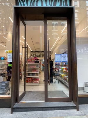 Double glass doors with brown metal frames. Push from brown metal handles in center to open.