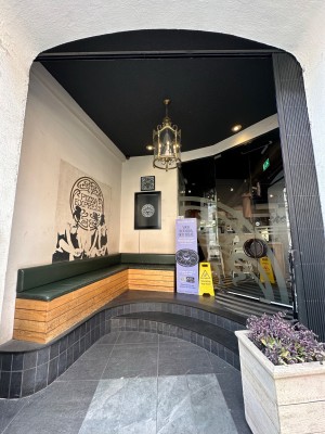 From pavement looking straight at opening ahead. Bench to far left. Entrance doors to far right. Both accessed via 2 steps.